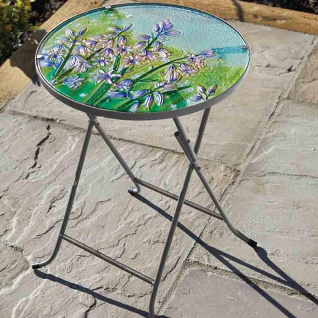 Sklenený stolík s ručne maľovanými kvetmi zvončekov na terase v záhrade